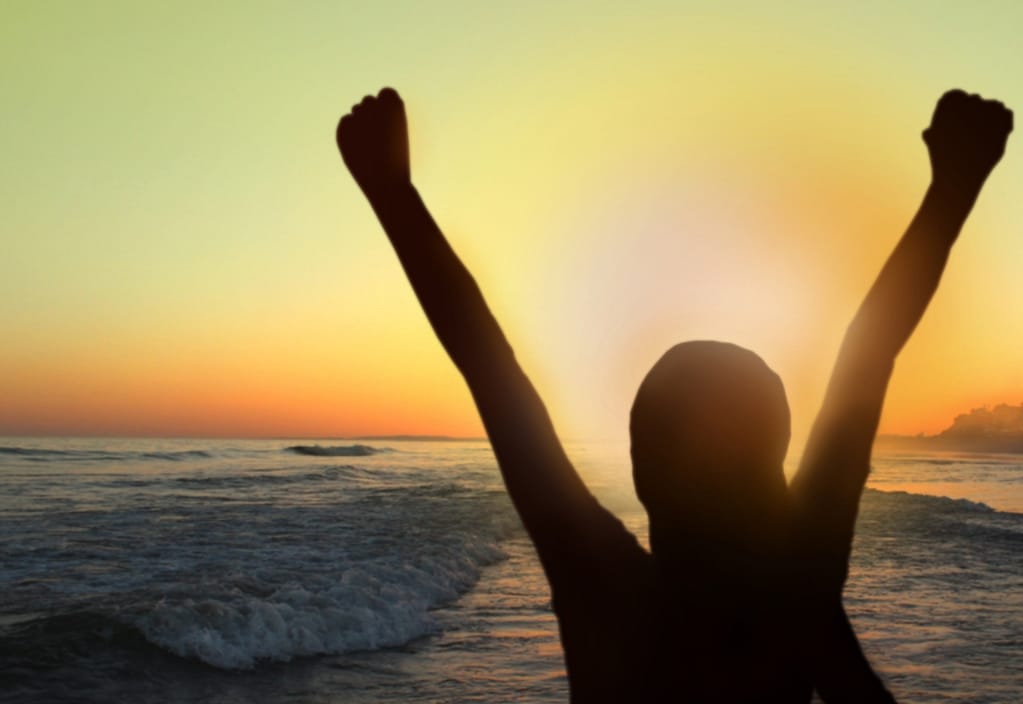 Woman with arms raised at sunset on the beach
