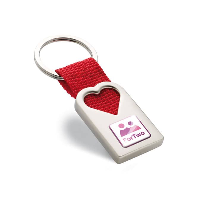 Key ring with logo BONHEUR Key ring with logo in metal, in mat pearl finish in hollow heart shape decoration. With polyester webbing holding the metal ring. Individual gift box. Available color: Red Dimensions: 5,5X2,5X0,6 CM Width: 2.5 cm Length: 5.5 cm Height: 0.6 cm Volume: 0.11 cdm3 Gross Weight: 0.036 kg Net Weight: 0.027 kg Depending on the surface we can use embroidery, engraving, 360Â° imprint or screen print.